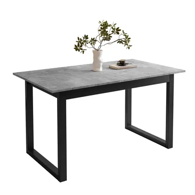 A dining table with a gray stone-like top and black metal U-shaped legs, with a vase of greenery and a book on top.