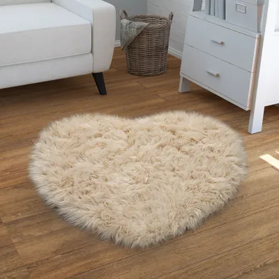 A heart-shaped fluffy rug on a wooden floor next to a white sofa and a dresser.