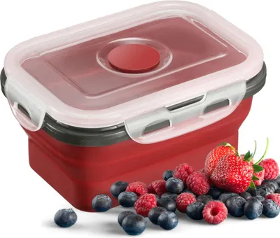 A red collapsible food container with a clear lid is shown with a pile of berries in front of it.