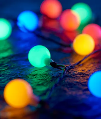 A close-up of a string of colorful LED lights on a dark, textured surface.