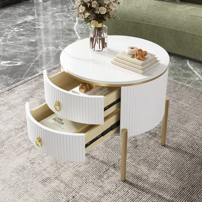 A white round side table with two drawers, decorated with a vase of flowers and books on top, placed on a rug in a living room.