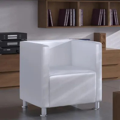 A white cube armchair is shown in a room with wooden furniture and shelves filled with books.
