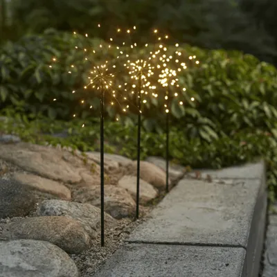 Three LED firework-shaped lights are placed in a garden setting along a stone pathway.