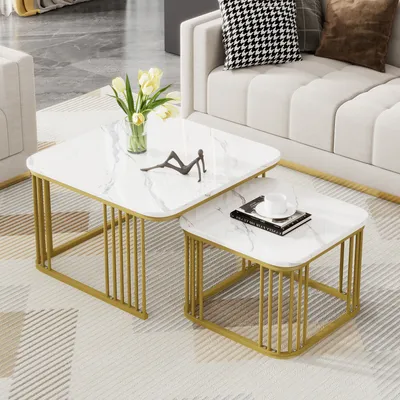 A set of two nesting square coffee tables with a white marble-look top and gold metal legs, placed in a living room setting next to a sofa.