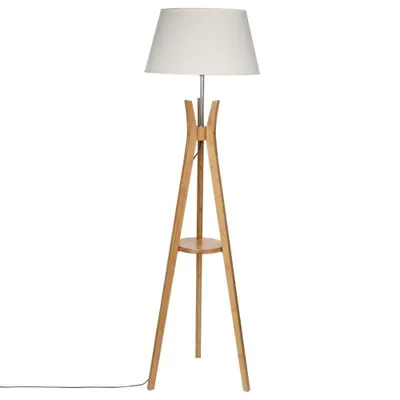 A floor lamp with a white shade and a wooden tripod base with a small shelf.