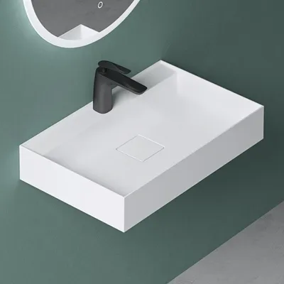 A white rectangular sink with a black faucet is mounted on a teal wall.