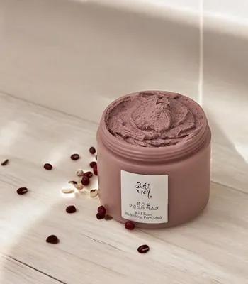 A jar of red bean refreshing pore mask is placed on a light-colored wooden surface, with scattered red beans around it.