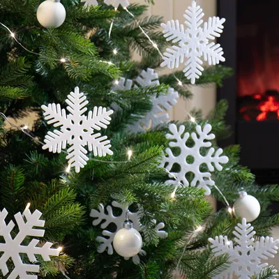 A close-up view of a decorated Christmas tree with white snowflake ornaments and string lights, with a fireplace visible in the background.