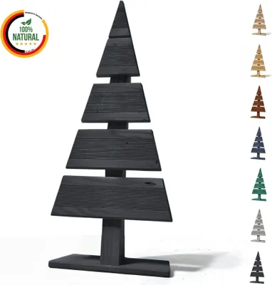 A dark-colored, stylized Christmas tree decoration made of wood, with several smaller versions of the same decoration in different colors lined up on the right side of the image. A circular badge with German flag colors and text '100% NATURAL' is in the to
