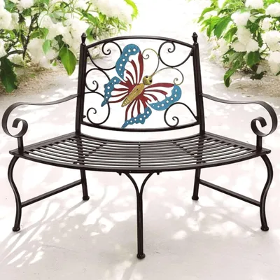A metal garden bench with a butterfly design on the back, placed outdoors with white flowers in the background.