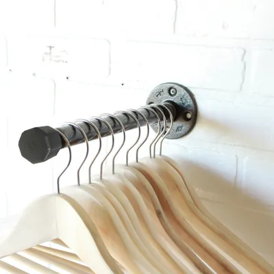 A pipe-style wall-mounted coat rack with wooden hangers attached, mounted on a white brick wall.