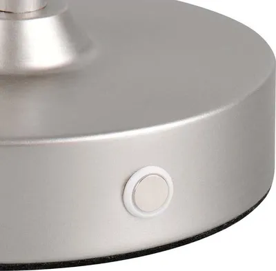 A close-up view of the base of a brushed nickel table lamp, showing a small touch-sensitive button.