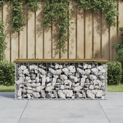 A gabion bench with a wooden top sits on a paved patio in front of a wooden fence with greenery.
