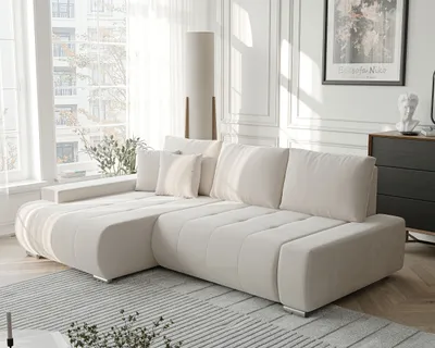 A modern living room with a beige sectional sofa, a floor lamp, and a window with sheer curtains.