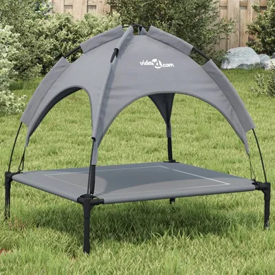 A dog bed with a canopy is set up on a grassy lawn in a backyard.