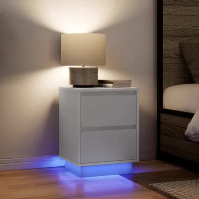 A white nightstand with two drawers and LED lighting at the base, next to a bed.