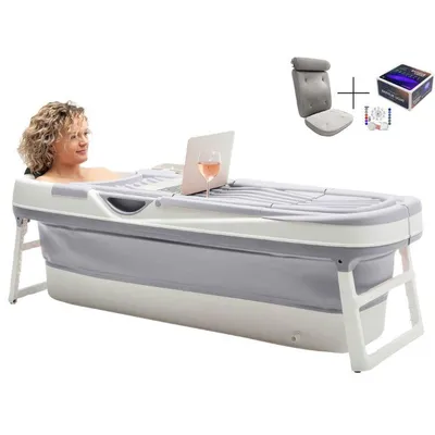 A woman is relaxing in a portable bathtub with a laptop and a glass of wine.