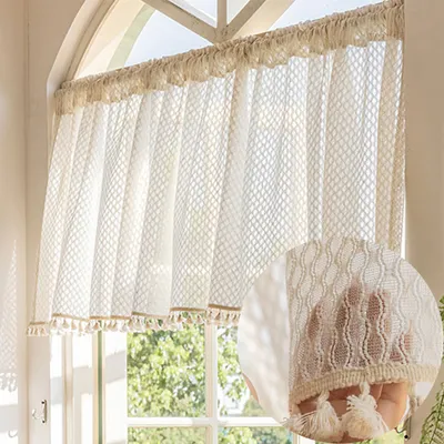 A close-up of a cream-colored lace curtain with tassels, showing the texture and detail of the fabric.