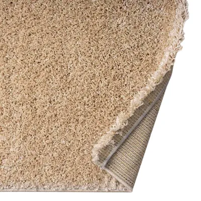 A close-up view of a beige shaggy rug, with a corner lifted to show the backing.