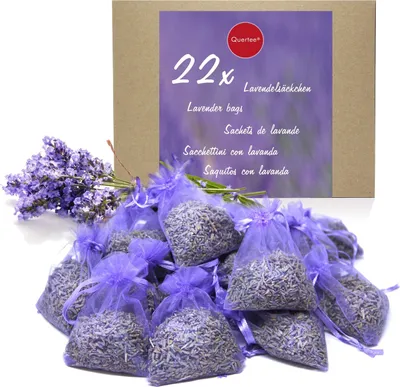 A box of lavender sachets with a bunch of lavender flowers and a pile of sachets in front.