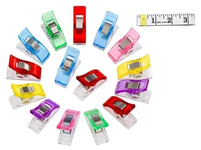 A collection of colorful sewing clips arranged in a circular pattern, with a small measuring tape in the upper right corner.