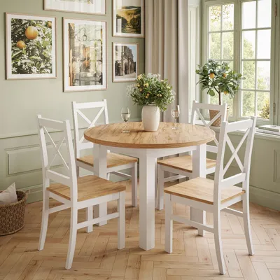 A dining set with a round wooden table and four white chairs in a room with light green walls and a window.