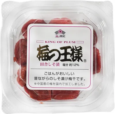 A clear, top-down view of a plastic container filled with pickled plums (umeboshi). A label is prominently displayed on the front of the container.