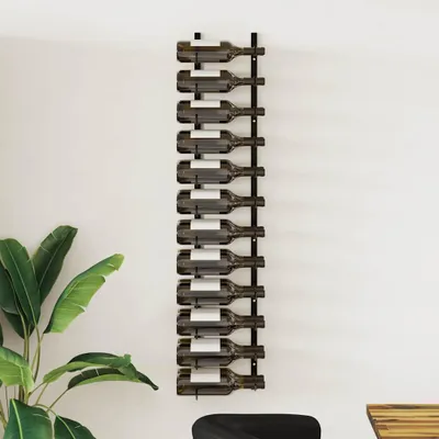A black metal wine rack mounted on a white wall, holding multiple wine bottles. A large green plant is visible to the left.