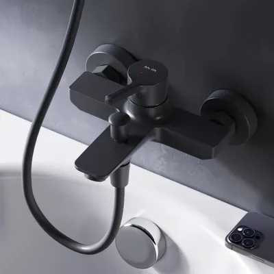 A black bathtub faucet mounted on a gray tiled wall above a white bathtub.
