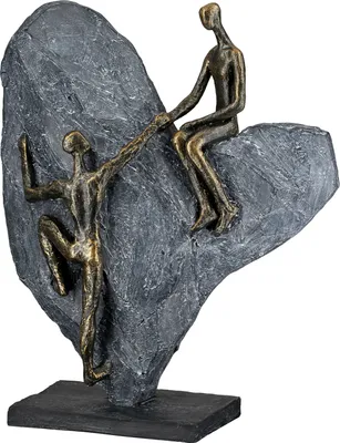 A sculpture of two figures climbing a rock, one reaching down to help the other.