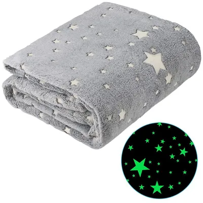A folded grey blanket with white stars is shown against a white background. A circular inset shows a close-up of the blanket's pattern glowing green in the dark.