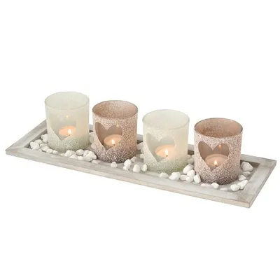 A set of four glass candle holders with heart cutouts, placed on a wooden tray with decorative stones.