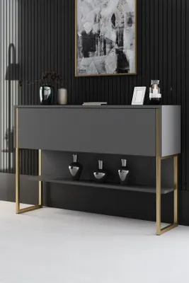A modern console table with gold legs and an anthracite top, displayed in a room with a black slatted wall and abstract art.