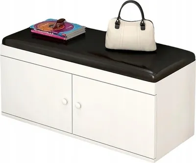 A white shoe cabinet with a black cushioned top, a stack of books, and a cream handbag on top.