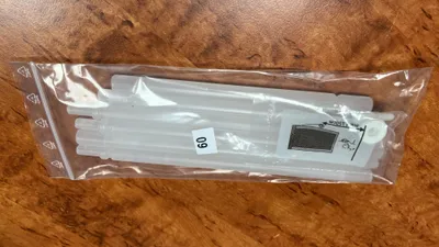 A clear plastic bag containing several white plastic rods, likely for a curtain or blind system, is placed on a wooden surface.