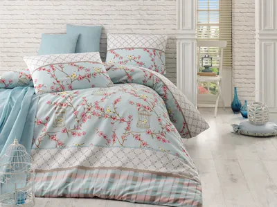 A beautifully made bed with a duvet cover featuring a floral and birdcage pattern, set against a white brick wall.