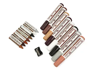 A collection of furniture repair markers and wax crayons arranged diagonally on a white background, with a small pencil sharpener.