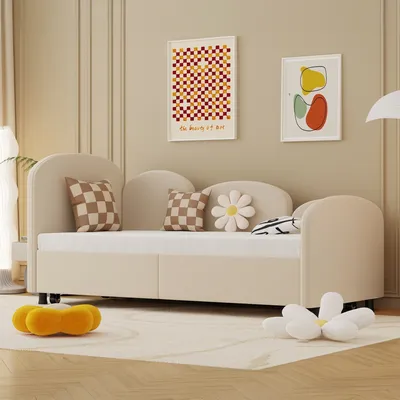 A beige daybed with pillows and decorative flower-shaped cushions on a rug in a room with artwork on the wall.
