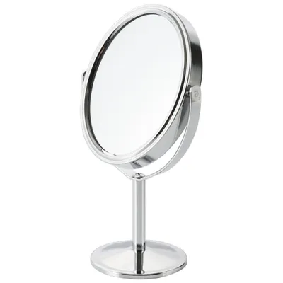 A silver makeup mirror on a stand against a white background.
