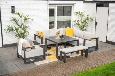 An outdoor lounge set with a sectional sofa, armchair, table, and bench on a patio with plants.