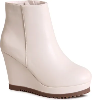 A studio shot of a single beige wedge ankle boot.