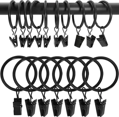 A set of black curtain rings with clips arranged on a black curtain rod and a white background.