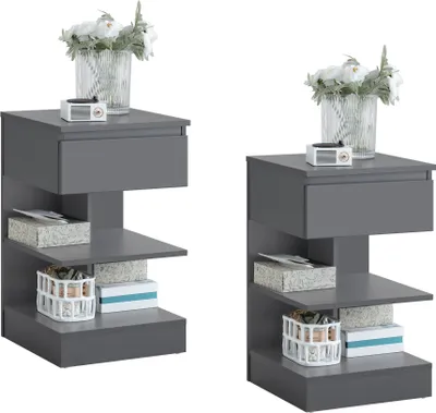 Two identical gray nightstands are displayed side-by-side against a white background. Each nightstand features a drawer and two open shelves, with decorative items like a vase of flowers, a small radio, boxes, and a basket on the shelves.