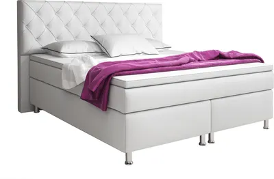 A white boxspring bed with a tufted headboard, white pillows, and a purple throw blanket.