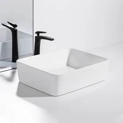 A white ceramic vessel sink with a black faucet is shown on a white countertop with a mirror reflection.