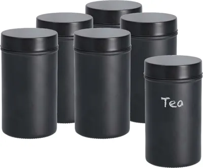 A set of six black storage jars with lids, arranged in a group. One jar in the foreground has the word 'Tea' written on it in white chalk.