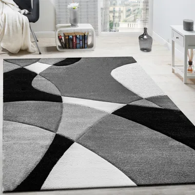 A modern geometric rug in black, white, and gray is displayed in a living room setting.