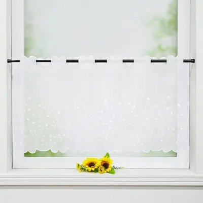 A white sheer curtain with a leaf pattern hangs in a window, with two sunflowers placed on the windowsill below.