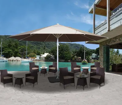 An outdoor patio scene with a large umbrella and seating area overlooking a body of water with boats and a building.