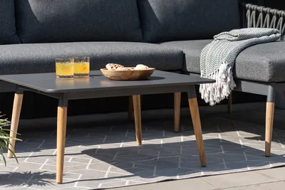 An outdoor coffee table with drinks and a bowl of snacks on it, placed on a rug in front of a sofa.